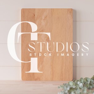 May include: A light brown wooden cutting board with the text "GT STUDIOS STOCK IMAGERY" printed on it. The board is sitting on a light wood surface with a sprig of green eucalyptus leaves in the foreground.
