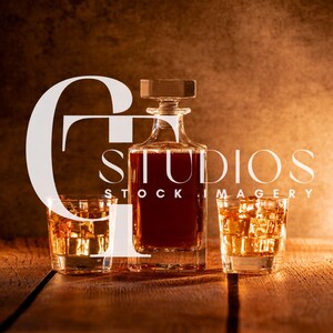 May include: A clear glass decanter with a square stopper, filled with amber liquid, stands between two glasses of whiskey with ice cubes. The image has the text "STUDIOS STOCK IMAGERY" in white.