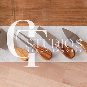 May include: Four cheese knives with wooden handles on a white marble surface. The knives are arranged in a row, with the handles facing the viewer. The knives are made of stainless steel and have a variety of shapes and sizes.