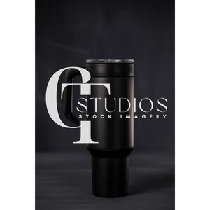 Puede incluir: Un termo de viaje de acero inoxidable negro con asa y tapa. El termo está sobre una superficie gris oscuro. "GT Studios Stock Imagery" está impreso en la superficie detrás del termo.
