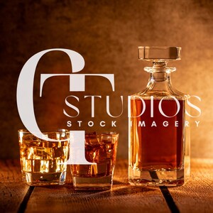 May include: A clear glass decanter with a square stopper and two square glasses filled with amber liquid and ice cubes. The image includes the text "STUDIOS STOCK IMAGERY" in white.