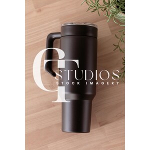 May include: A black stainless steel travel mug with a handle. The mug has a black lid and is sitting on a wooden surface.