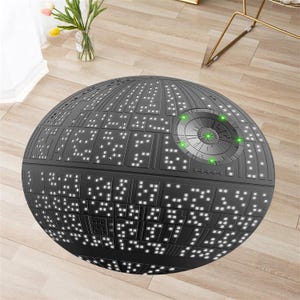 May include: A black and white round rug with a design that resembles the Death Star from Star Wars. The rug has a circular design with a central hub and multiple panels radiating outwards. The rug is on a wooden floor.