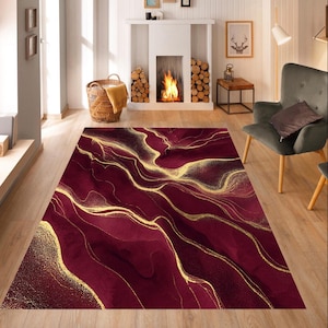 Könnte beinhalten: Ein rechteckiger Teppich mit einem abstrakten Design in Burgunderrot und Gold. Der Teppich weist fließende, marmorierte Muster in tiefem Rot und schimmerndem Gold auf, die eine luxuriöse und künstlerische Ästhetik erzeugen. Der Teppich liegt auf einem Holzboden in einem Wohnzimmer.