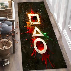 Peut inclure: Tapis rectangulaire avec un fond sombre et un motif composé d'un carré, d'un triangle et d'un cercle dorés, avec des éclaboussures de peinture rouge, jaune et verte. Le tapis est probablement fait d'un matériau durable.