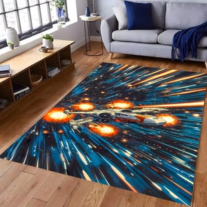 Puede incluir: Una alfombra rectangular con una escena de batalla espacial con un caza estelar. La alfombra tiene un fondo azul y negro con rayas naranjas y blancas, y una imagen detallada de un caza estelar.