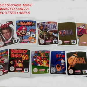 Peut inclure: Une collection d'étiquettes de jeux vidéo laminées et prédécoupées, avec des titres tels que Super Smash Bros, Zelda et Donkey Kong 64. Les étiquettes présentent des graphismes colorés et le texte "PROFESSIONAL MADE - LAMINATED LABELS - PRECUTTED LABELS".