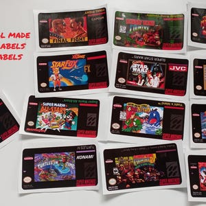 Könnte beinhalten: Eine Sammlung laminierter und vorgeschnittener Super Nintendo-Spieleetiketten. Die Etiketten zeigen farbenfrohe Grafiken und Texte aus verschiedenen klassischen Spielen, darunter "Final Fight", "Star Fox" und "Super Mario All-Stars".