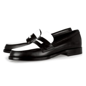 May include: Black leather loafers with a white leather panel across the toe. The loafers have a classic penny loafer design with a single strap across the top.
