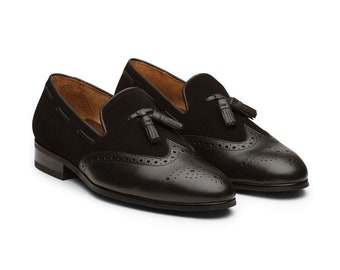 May include: Black leather loafers with a suede toe and tassel detail. The loafers have a brogue pattern and a rounded toe.