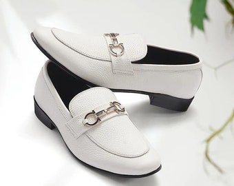 May include: A pair of white leather loafers with gold buckle accents. The loafers have a pointed toe and a low heel.