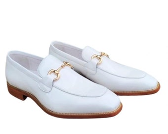 May include: A pair of white leather loafers with gold chain detailing and a brown sole.