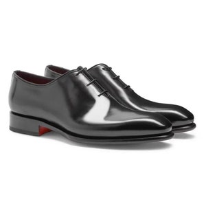 Op de afbeelding: Zwarte leren veterschoenen met een spitse neus en een rode zool.
