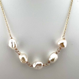 May include: A gold chain necklace with five white baroque pearls. The pearls are irregularly shaped and have a natural, organic look.
