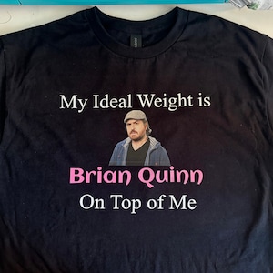 May include: Black t-shirt with white text that reads "My Ideal Weight is Brian Quinn On Top of Me". A photo of Brian Quinn is printed on the shirt.
