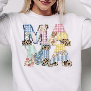 Könnte beinhalten: Weißes Sweatshirt mit dem Wort "MAMA" auf der Vorderseite appliziert. Die Buchstaben bestehen aus Patchwork-Stoff in verschiedenen Mustern, darunter Blumen-, Vichy- und Leopardenmuster. Das Sweatshirt hat lange Ärmel und einen Rundhalsausschnitt.