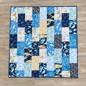 May include: A blue and white patchwork quilt with a nautical theme. The quilt features images of whales, seahorses, fish, and seashells. The quilt is made of various fabrics with different textures and patterns. The quilt is edged with a dark blue fabric.