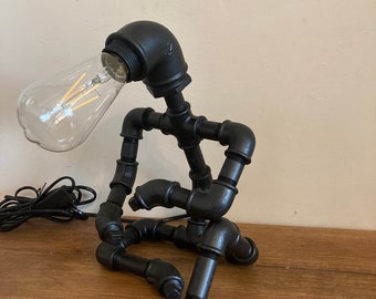 Steam punk style metal lamp depicting a person sitting down and leaning on their knee.