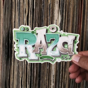 May include: A green, white, and brown sticker with the word "RAZD" written in a graffiti style font. The sticker is being held by a hand in front of a wall of vinyl records.