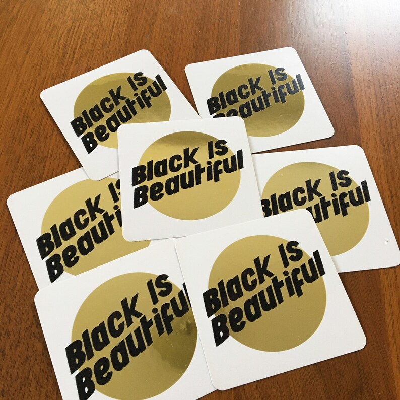 May include: Eight square stickers with gold foil accents and the text "Black is Beautiful" in black lettering.