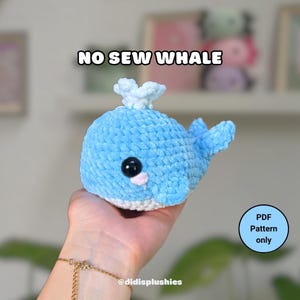 May include: A light blue crocheted whale plushie with black safety eyes and a small pink mouth. The whale has a white belly and a small spout. Text on the image reads "NO SEW WHALE" and "PDF Pattern only".