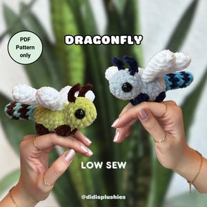Peut inclure: Deux peluches de libellule crochetées, l'une verte et marron, l'autre bleue et blanche. Les peluches sont tenues dans les mains de deux personnes. Le texte "DRAGONFLY" et "LOW SEW" est visible sur l'image. Le texte "PDF Pattern only" est dans un cercle.