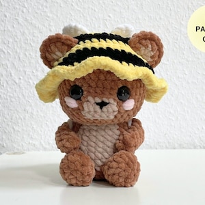 May include: Crochet pattern for a brown teddy bear wearing a yellow and black striped bee hat. The pattern is available as a PDF download.