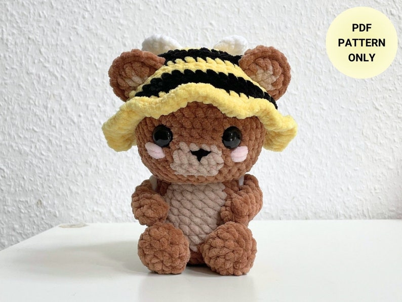 May include: Crochet pattern for a brown teddy bear wearing a yellow and black striped bee hat. The pattern is available as a PDF download.