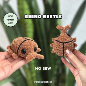Könnte beinhalten: Zwei braune gehäkelte Nashornkäfer-Plüschtiere. Der Käfer links hat einen langen Rüssel und der Käfer rechts hat ein Horn. Der Text "RHINO BEETLE" befindet sich oben im Bild. Der Text "NO SEW" befindet sich in der Mitte des Bildes. Der Text "@didisplushies" befindet sich unten im Bild.