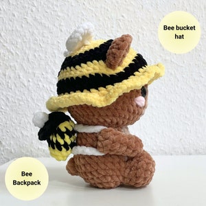 May include: A brown crocheted plush toy wearing a yellow and black bee bucket hat and a yellow and black bee backpack.