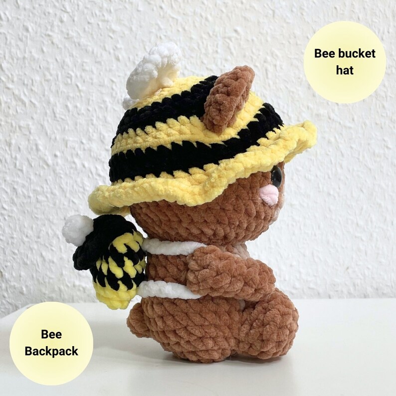 May include: A brown crocheted plush toy wearing a yellow and black bee bucket hat and a yellow and black bee backpack.