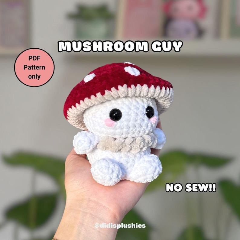 Op de afbeelding: Een handgemaakte gehaakte paddenstoelknuffel met een rode en wit gestippelde kap, witte body en zwarte ogen. De tekst "MUSHROOM GUY" en "NO SEW!!" worden weergegeven. De knuffel wordt in een hand gehouden. De tekst "PDF Pattern only" en "@didisplushies" zijn ook zichtbaar.