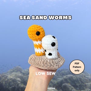 Könnte beinhalten: Zwei gehäkelte Meeressandwürmer auf einer beigen Basis. Ein Wurm ist orange-weiß gestreift, der andere ist weiß mit schwarzen Punkten. Beide haben schwarze Sicherheitsaugen. Text: SEA SAND WORMS, LOW SEW und PDF Pattern only.