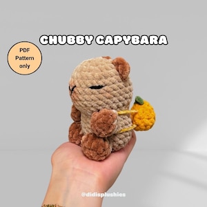 Może przedstawiać: Szydełkowana pluszowa kapibara w odcieniach brązu, trzymająca żółty owoc z zielonym liściem. Tekst "CHUBBY CAPYBARA" znajduje się nad pluszakiem. Okrągła grafika głosi "PDF Pattern only". Widoczna jest nazwa sklepu Etsy.