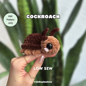 Peut inclure: Un jouet en peluche en forme de cafard crocheté brun et beige avec de grands yeux noirs. Le jouet est tenu par une main avec des anneaux dorés. Le texte "COCKROACH" est au-dessus du jouet et "LOW SEW" est en dessous du jouet. Le texte "PDF Pattern only" est dans un cercle en haut à gauche de l'image. Le texte "@didisplushies" est en dessous du jouet.