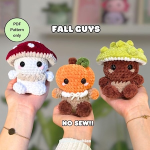 Könnte beinhalten: Drei gehäkelte Plüschtiere in Form von Pilzen und einem Kürbis. Die Pilzspielzeuge sind weiß mit roter und weißer Kappe und braun mit grüner Kappe. Der Kürbis ist orange. Der Text lautet "FALL GUYS" und "NO SEW!!".