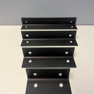 May include: Four black metal L-shaped brackets with four holes each. The brackets are arranged in a vertical stack.