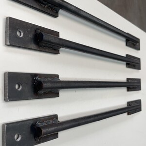 May include: Four black metal drawer pulls with a rounded end and a single hole in the center of the rectangular base. The pulls are arranged in a row on a white surface.