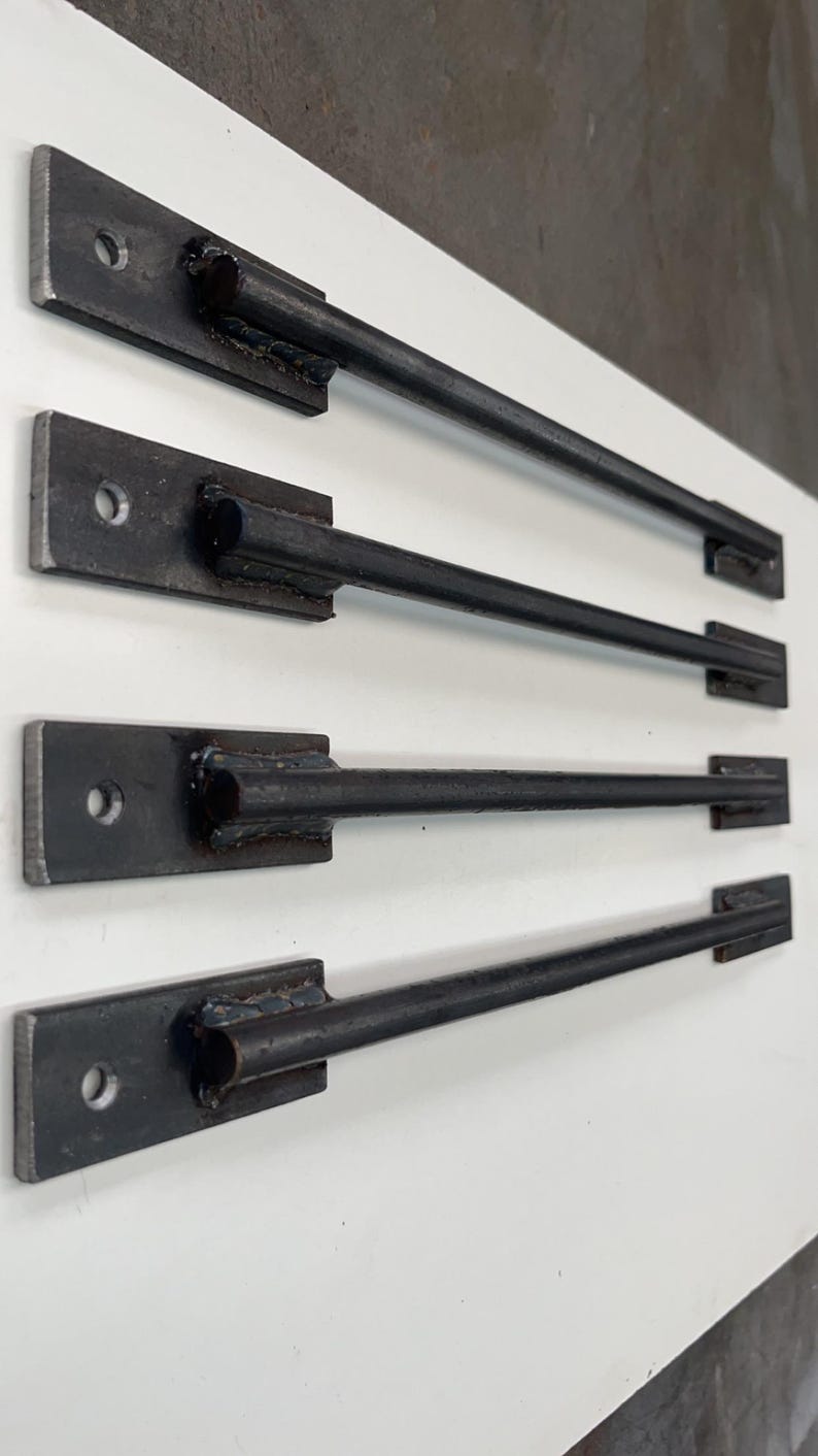May include: Four black metal drawer pulls with a rounded end and a single hole in the center of the rectangular base. The pulls are arranged in a row on a white surface.