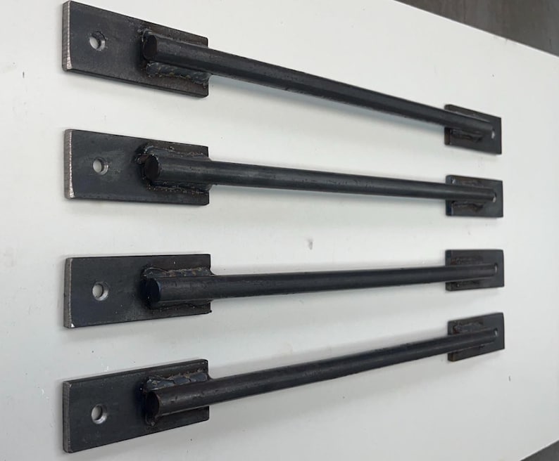 May include: Four black metal rods with flat ends, each with a hole drilled through the flat end. The rods are arranged vertically, with the top rod being the longest and the bottom rod being the shortest.