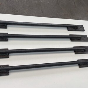 May include: Four black metal handles with a simple design. Each handle has a rectangular base and a straight bar.