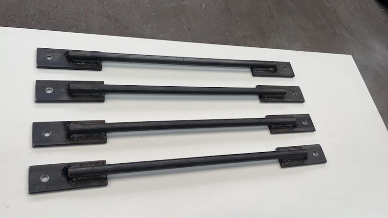 May include: Four black metal handles with a simple design. Each handle has a rectangular base and a straight bar.