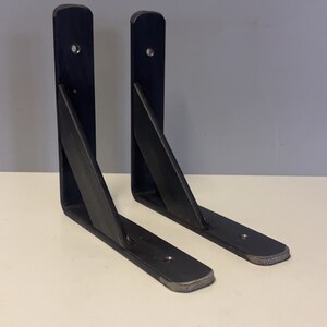 May include: A pair of black metal shelf brackets. Each bracket features a vertical support and a horizontal shelf, joined by a diagonal brace. The brackets are made of robust metal and are designed for wall mounting.