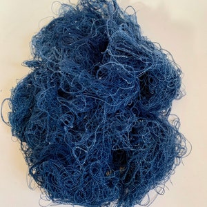 May include: A pile of dark blue thread, tightly wound and tangled, creating a textured, irregular shape. The threads appear to be made of a fine, possibly synthetic material, with a slight sheen. The threads are densely packed, suggesting a substantial amount of material.