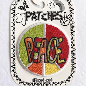 May include: A circular embroidered patch featuring a segmented background of lime green, red, orange, and yellow. The word PEACE is stitched in bold, multi-colored letters across the center. The patch is mounted on a white card labeled PATCHES.