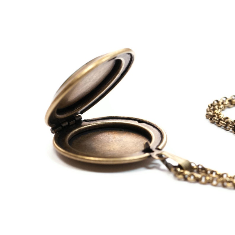 May include: A gold-toned locket necklace with a hinged lid open, revealing an empty interior. The chain is made of small, linked circles.