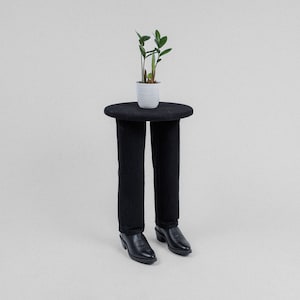 May include: A black side table with a round top and legs shaped like a pair of pants. A small potted plant sits on the table top.