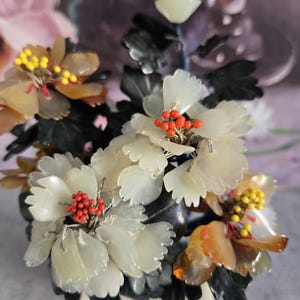 May include: A jade and agate flower arrangement in a white pot. The flowers are made of white jade and have red and yellow accents. The leaves are made of black jade.