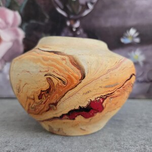May include: A small, round, ceramic vase with a marbled design in shades of brown, orange, and red. The vase has a smooth, glossy finish.