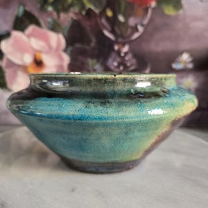 May include: A small, teal-colored ceramic bowl with a glossy finish. The bowl has a rounded bottom and a slightly flared rim.